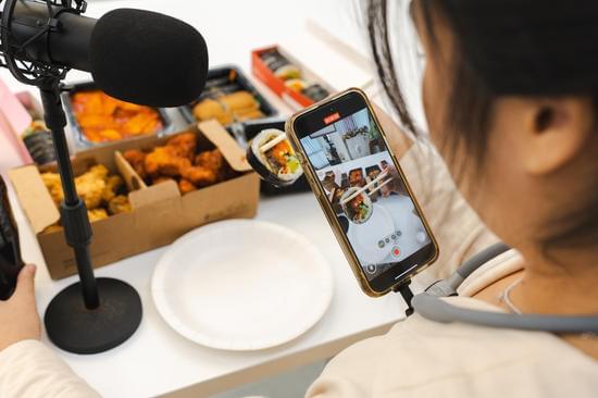 “Young female livestreamer surrounded by large amounts of food during online broadcast”